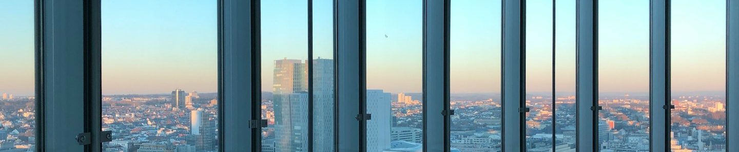 City skyline viewed through tall office space windows at sunset.