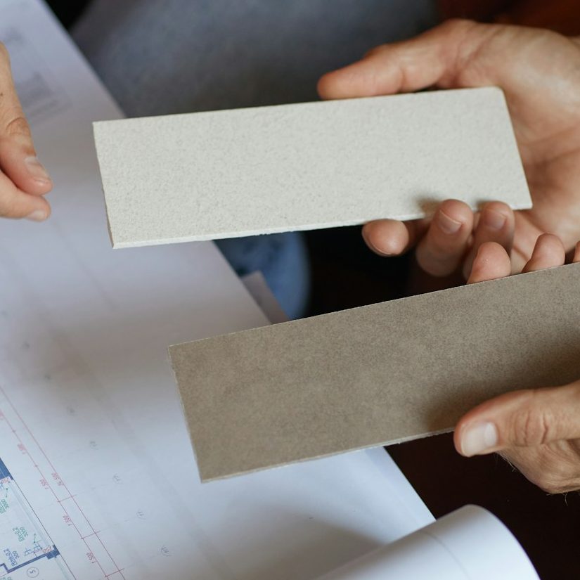 Hands holding color samples over an office design blueprint.