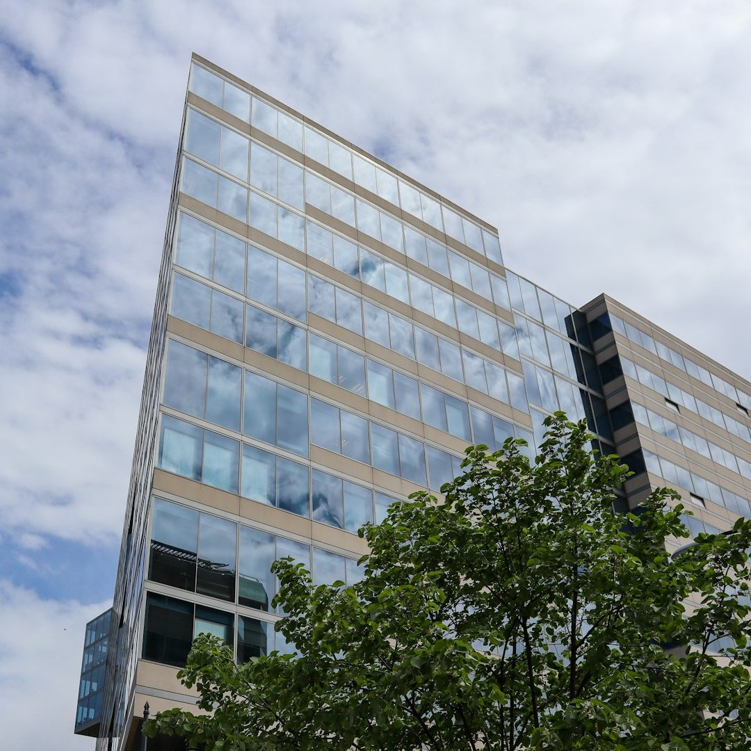 Office Solutions Modern glass building with multiple stories, partially surrounded by trees.